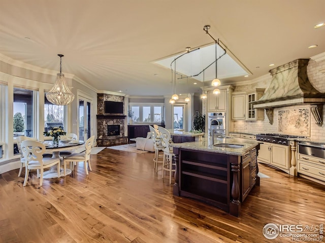 kitchen featuring a stone fireplace, hardwood / wood-style floors, custom exhaust hood, light stone counters, and sink