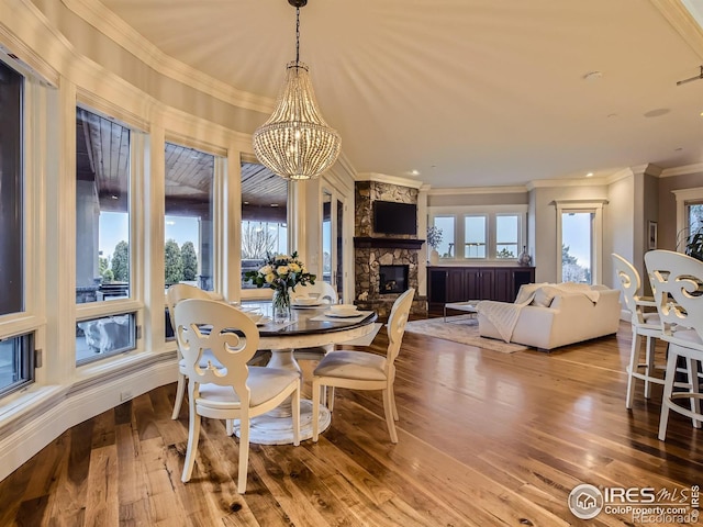 dining room featuring ornamental molding, an inviting chandelier, a stone fireplace, and wood-type flooring