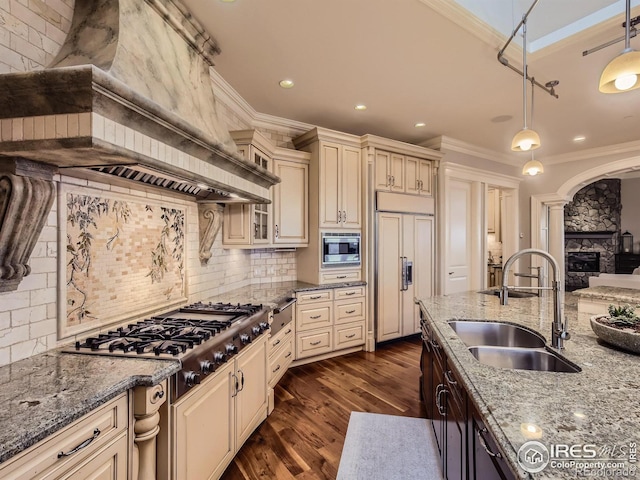 kitchen with decorative backsplash, built in appliances, pendant lighting, cream cabinets, and sink