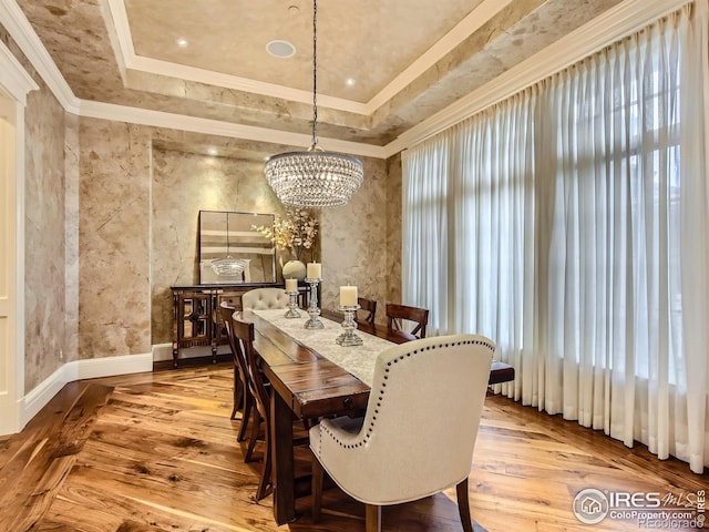 dining area featuring light wood-type flooring, a raised ceiling, ornamental molding, and a chandelier