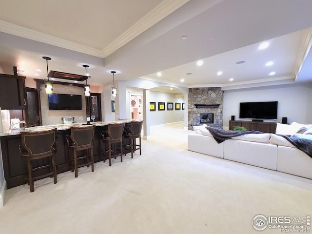 carpeted living room featuring a stone fireplace, ornamental molding, and a tray ceiling