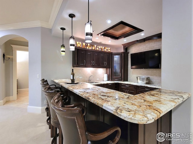 kitchen with backsplash, decorative light fixtures, dark brown cabinetry, light carpet, and kitchen peninsula