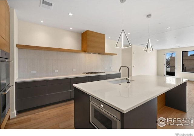 kitchen with pendant lighting, sink, light hardwood / wood-style flooring, an island with sink, and appliances with stainless steel finishes