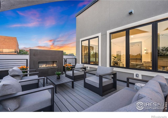 deck at dusk with an outdoor living space with a fireplace