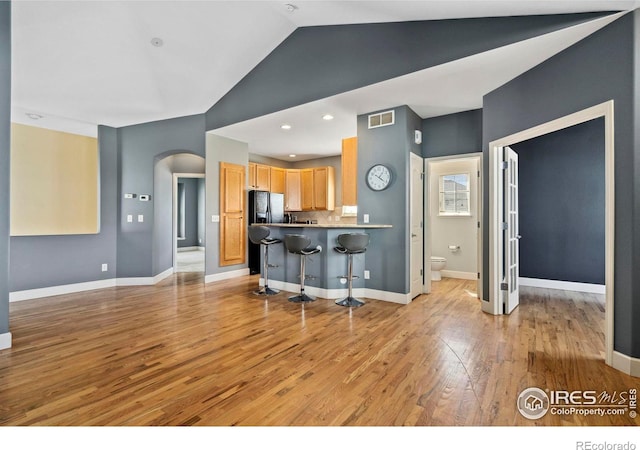 kitchen with light wood-type flooring, black fridge with ice dispenser, kitchen peninsula, and a kitchen bar