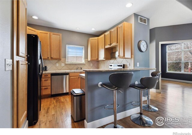 kitchen featuring black refrigerator, tasteful backsplash, stainless steel dishwasher, a kitchen bar, and light hardwood / wood-style flooring