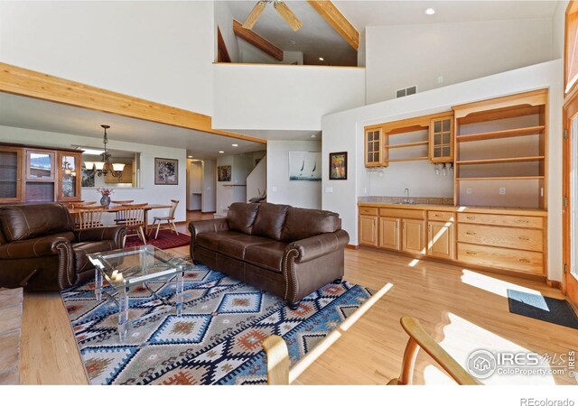 living room featuring beamed ceiling, ceiling fan, high vaulted ceiling, sink, and light wood-type flooring