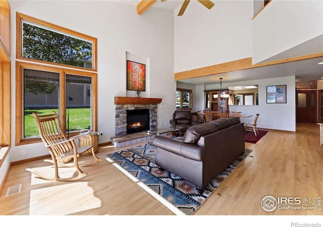 living room featuring a stone fireplace, ceiling fan, a towering ceiling, and light wood-type flooring