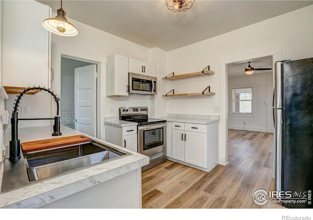 kitchen with appliances with stainless steel finishes, light hardwood / wood-style floors, hanging light fixtures, and white cabinetry