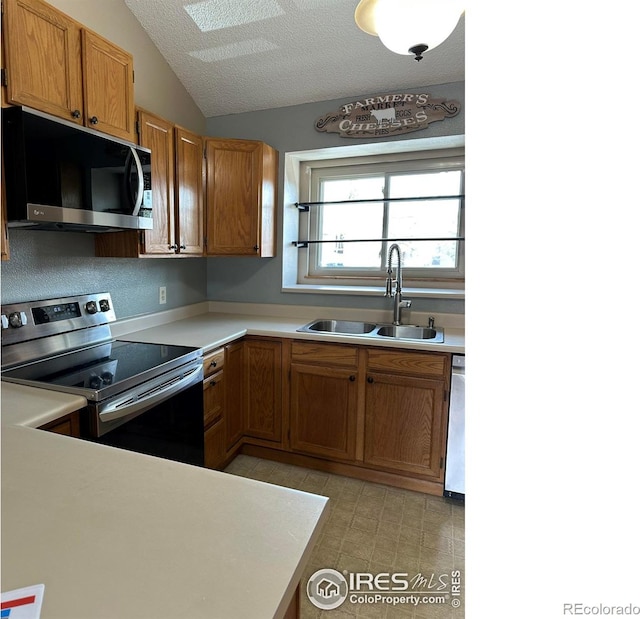 kitchen featuring vaulted ceiling, stainless steel appliances, light tile floors, sink, and a textured ceiling