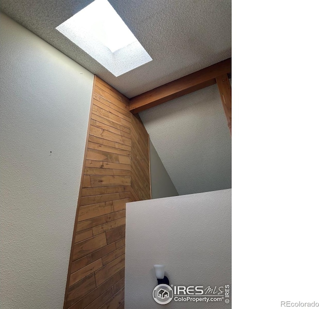 details featuring beamed ceiling, a textured ceiling, wooden walls, and a skylight