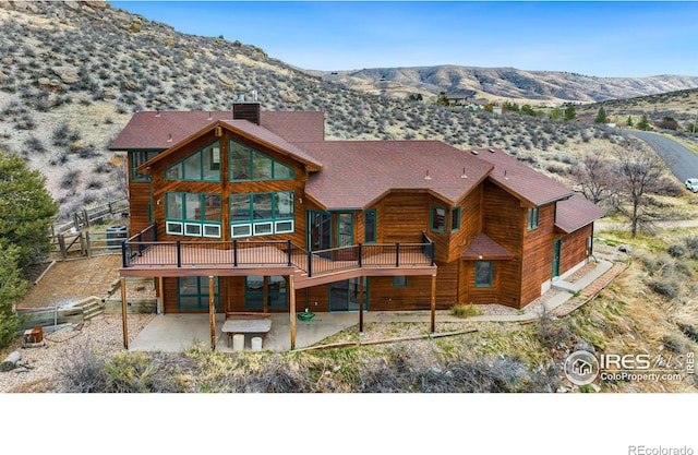 rear view of property featuring a deck with mountain view and a patio area