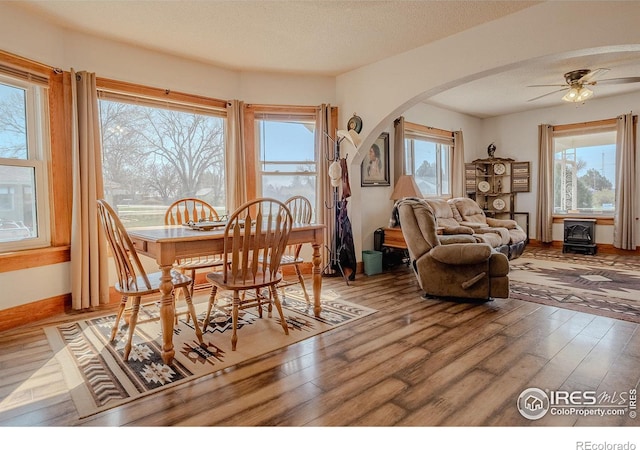 dining space with ceiling fan, a wood stove, a wealth of natural light, and hardwood / wood-style floors