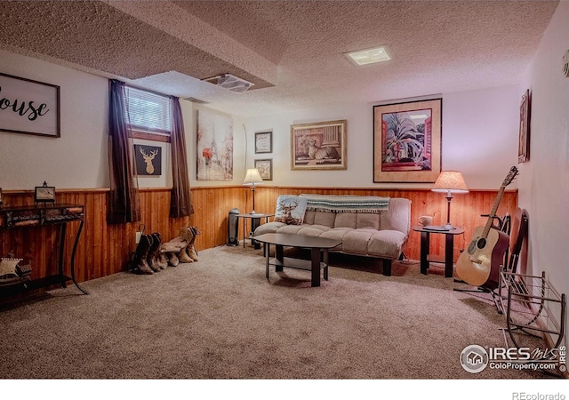 sitting room featuring carpet floors, wooden walls, and a textured ceiling