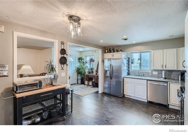 kitchen featuring a textured ceiling, backsplash, white cabinetry, and stainless steel appliances