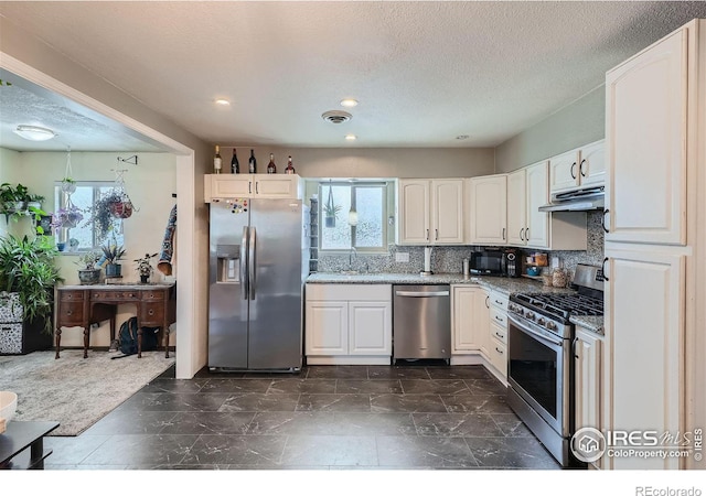 kitchen featuring stainless steel appliances, light stone counters, backsplash, a textured ceiling, and white cabinets