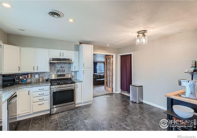 kitchen with white cabinets, appliances with stainless steel finishes, backsplash, and light stone countertops