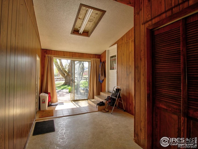 doorway with wood walls, a textured ceiling, lofted ceiling, and light tile patterned floors