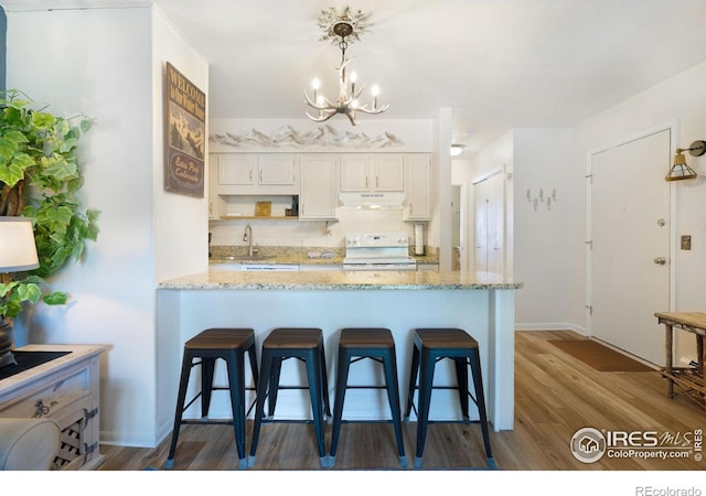 kitchen featuring white cabinetry, stove, hardwood / wood-style flooring, light stone counters, and sink