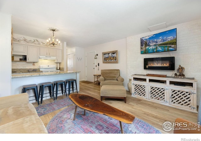 living room with a fireplace, brick wall, light wood-type flooring, and a chandelier