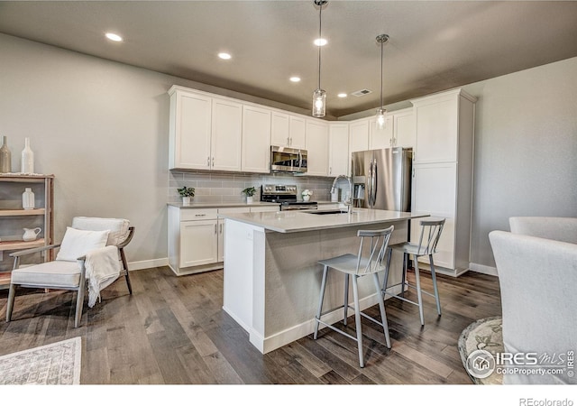 kitchen featuring appliances with stainless steel finishes, decorative light fixtures, white cabinetry, and hardwood / wood-style floors