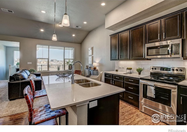 kitchen featuring lofted ceiling, a kitchen island with sink, stainless steel appliances, sink, and light hardwood / wood-style floors