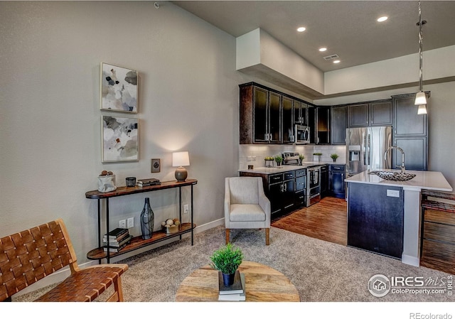 kitchen featuring decorative backsplash, a kitchen island with sink, stainless steel appliances, hardwood / wood-style flooring, and hanging light fixtures