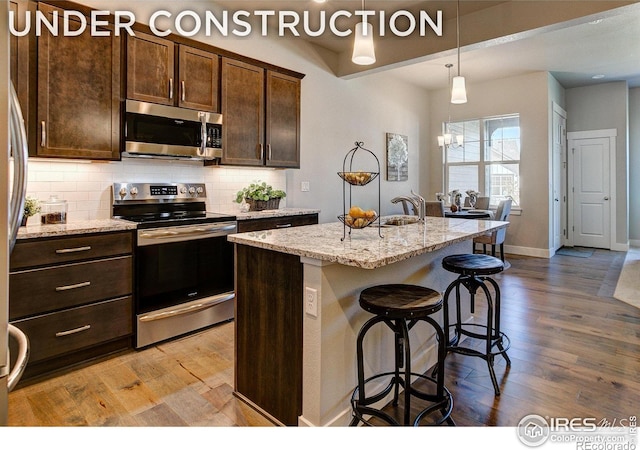 kitchen with light stone countertops, a kitchen island with sink, stainless steel appliances, and light wood-type flooring