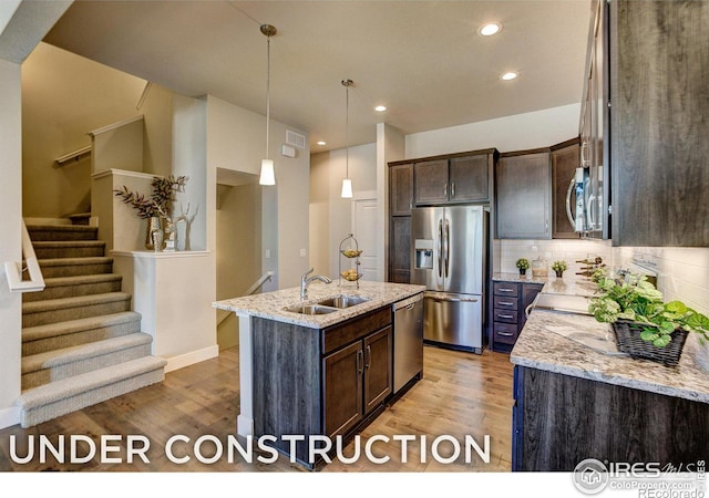 kitchen with light stone counters, stainless steel appliances, a kitchen island with sink, sink, and light hardwood / wood-style floors