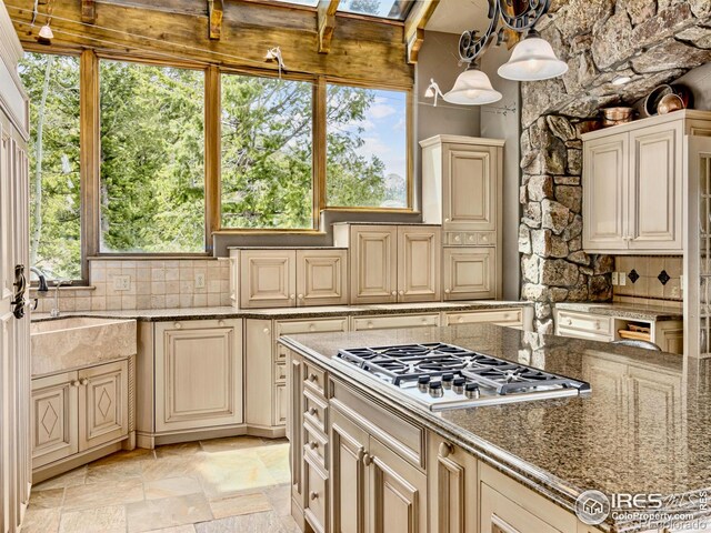 kitchen with tasteful backsplash, stainless steel gas cooktop, cream cabinets, and decorative light fixtures