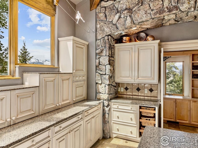 kitchen with light stone countertops, cream cabinetry, and tasteful backsplash