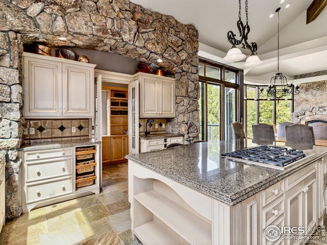 kitchen with dark stone counters, lofted ceiling, stainless steel gas cooktop, and a notable chandelier