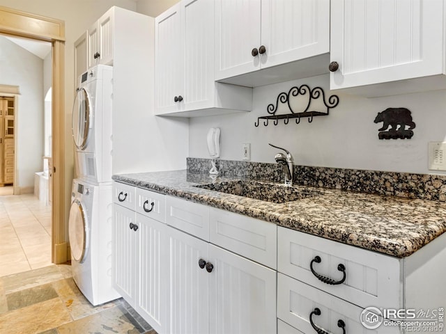 laundry area with cabinets, stacked washer / drying machine, and sink