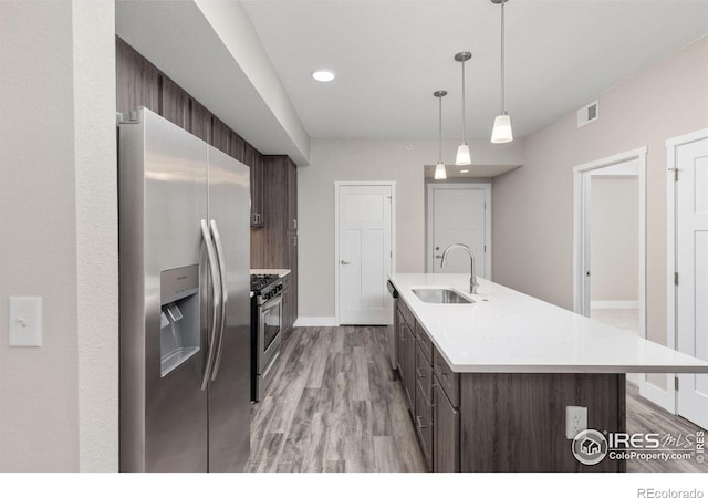 kitchen with stainless steel appliances, dark brown cabinets, sink, light wood-type flooring, and hanging light fixtures