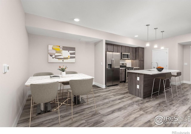 kitchen with a center island with sink, appliances with stainless steel finishes, a breakfast bar, sink, and dark brown cabinets