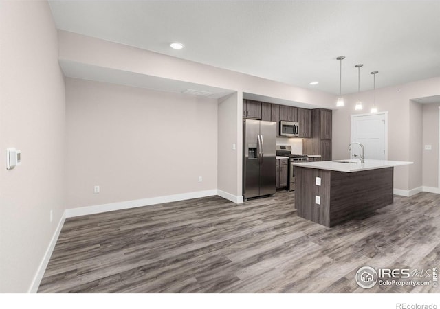 kitchen with appliances with stainless steel finishes, hanging light fixtures, dark brown cabinetry, an island with sink, and sink