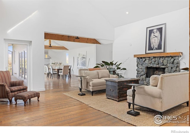 living room featuring vaulted ceiling with beams, a fireplace, and light hardwood / wood-style flooring