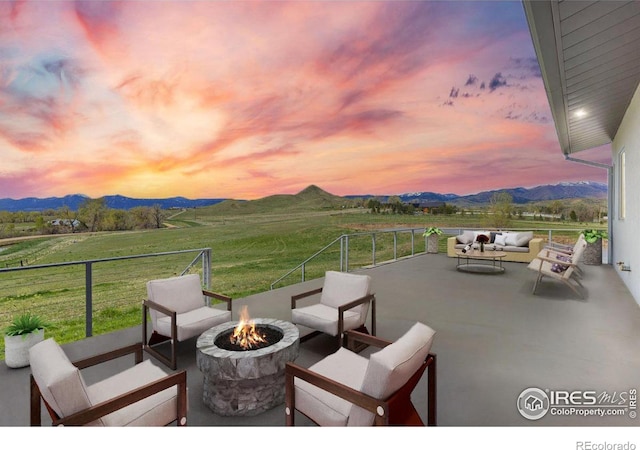 patio terrace at dusk featuring a balcony, a mountain view, a rural view, and an outdoor fire pit