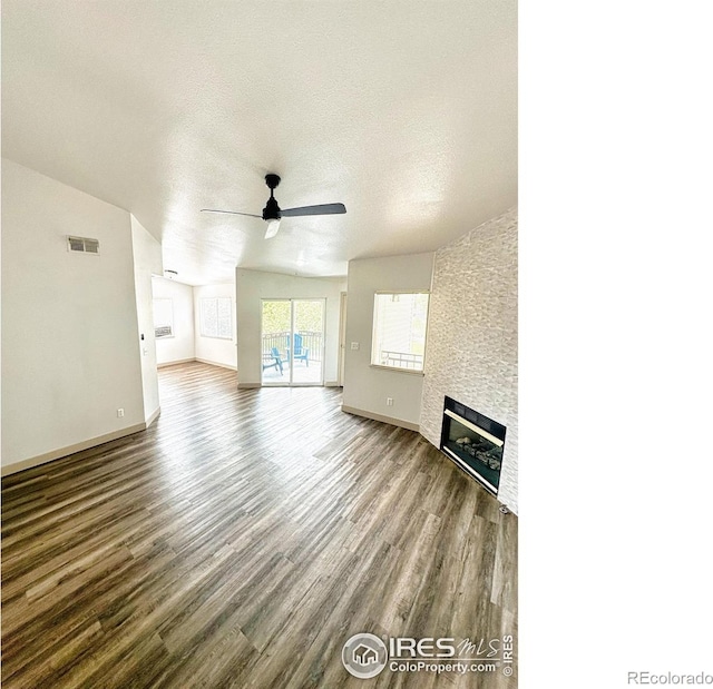 unfurnished living room with a large fireplace, visible vents, ceiling fan, wood finished floors, and a textured ceiling