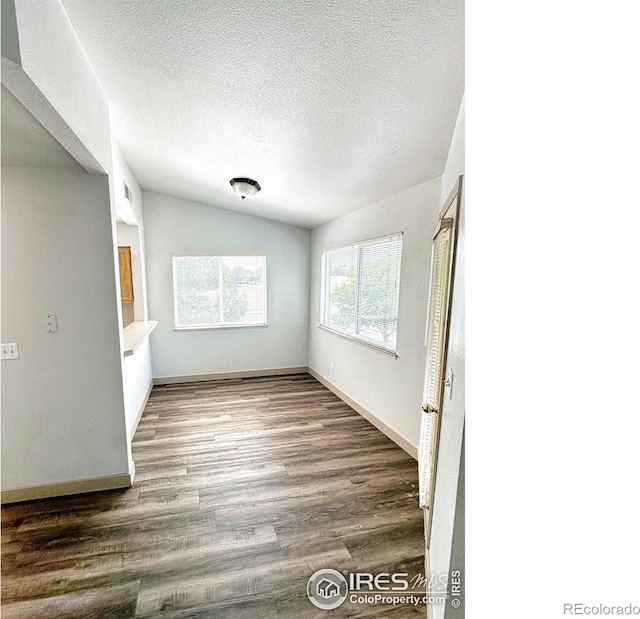 unfurnished room with wood-type flooring, vaulted ceiling, and a textured ceiling