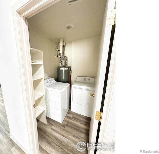 clothes washing area featuring hardwood / wood-style flooring, gas water heater, and washing machine and clothes dryer