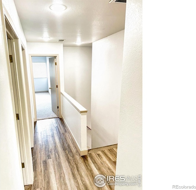 hall featuring visible vents, wood finished floors, an upstairs landing, and baseboards