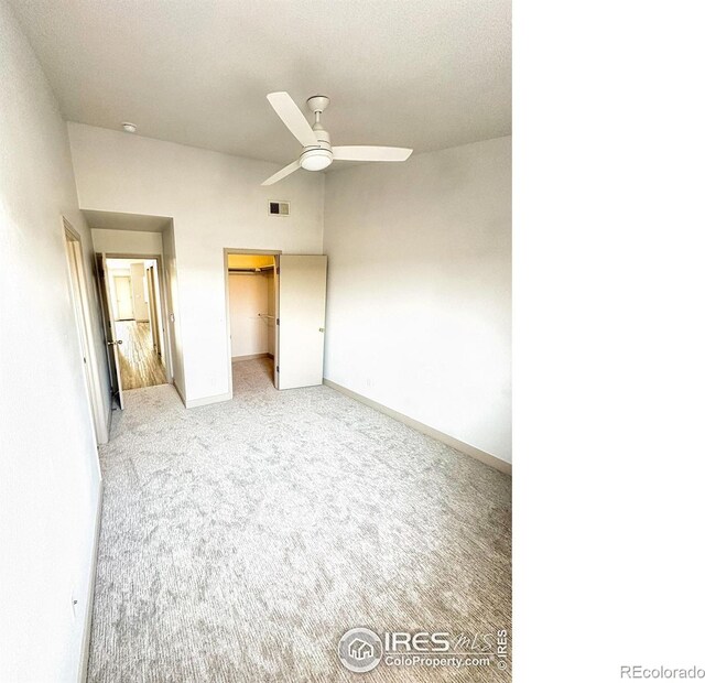 unfurnished bedroom featuring ceiling fan, carpet, a closet, and a walk in closet