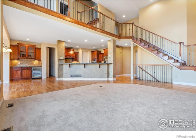 unfurnished living room featuring a towering ceiling, light hardwood / wood-style floors, and beverage cooler