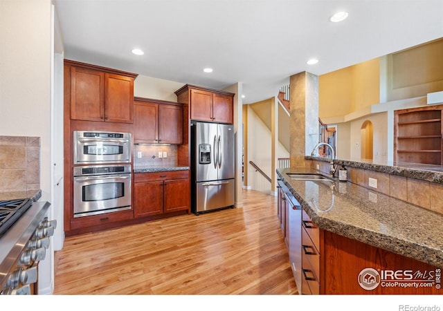 kitchen with sink, appliances with stainless steel finishes, dark stone counters, backsplash, and light wood-type flooring