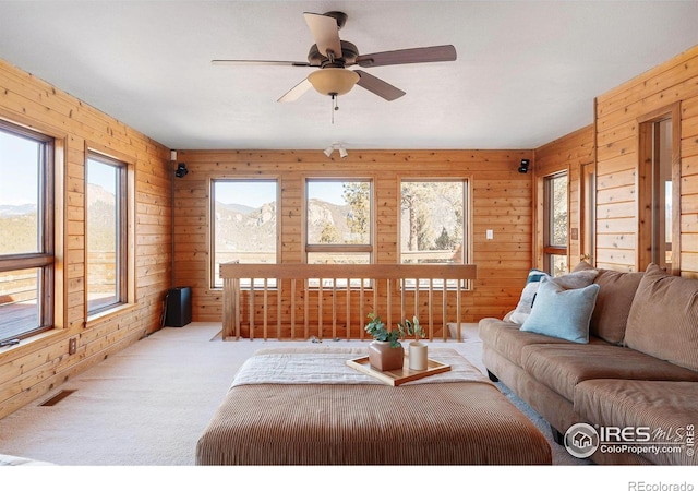 carpeted living room with wooden walls, visible vents, and a ceiling fan