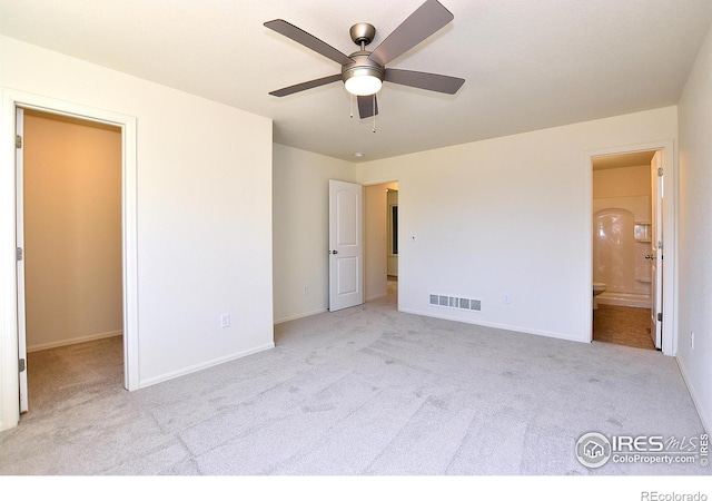 unfurnished bedroom featuring ceiling fan, light colored carpet, a walk in closet, and ensuite bath