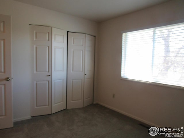 unfurnished bedroom featuring dark colored carpet and multiple windows