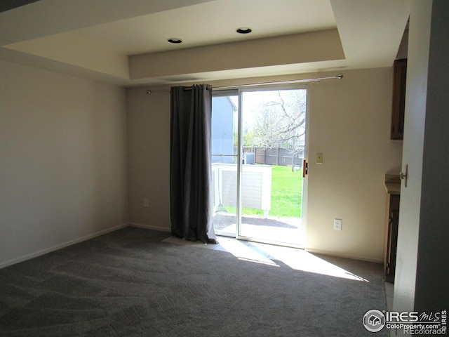 empty room with a tray ceiling and dark colored carpet