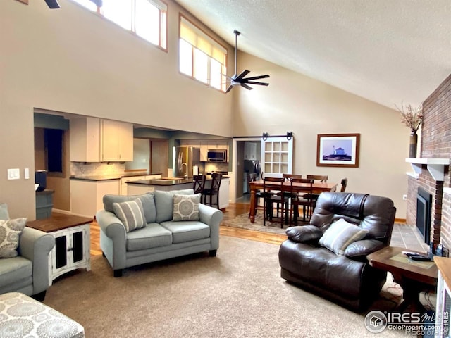 living room featuring ceiling fan, high vaulted ceiling, a textured ceiling, light carpet, and a fireplace